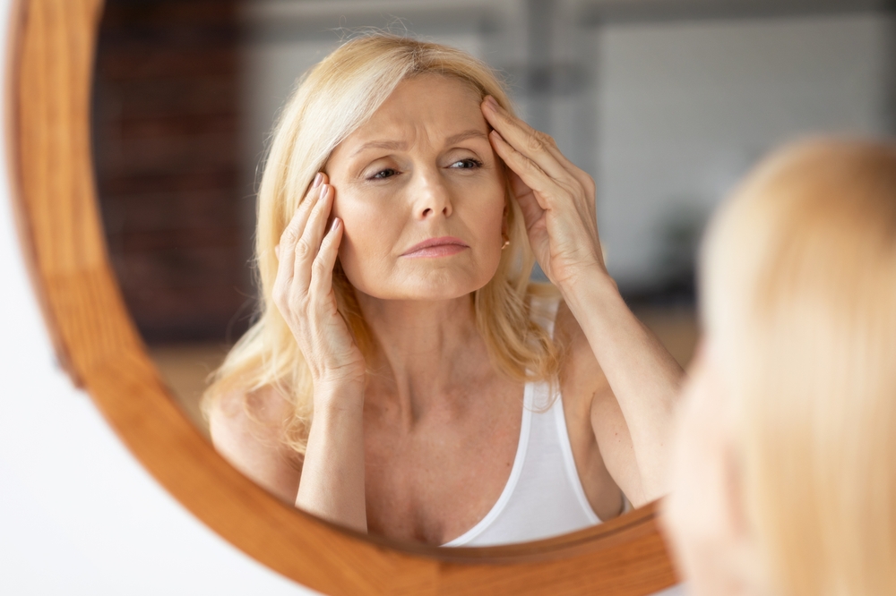 Upset,Middle,Aged,Woman,Looking,At,Mirror,And,Touching,Wrinkles